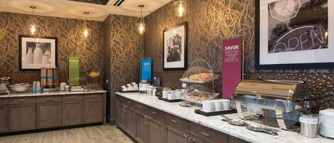 A breakfast bar with a coffee machine, a sandwich display, and various breakfast items.