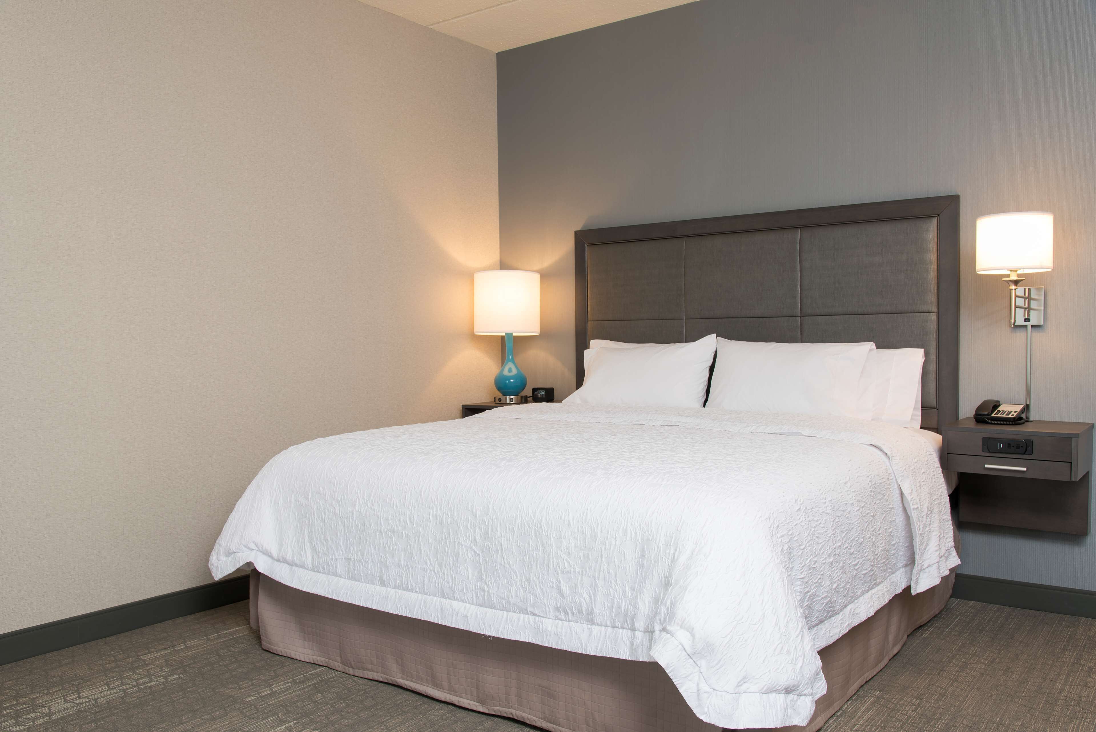 A hotel room with a large bed, a nightstand with a lamp, and a bedside table with a phone.