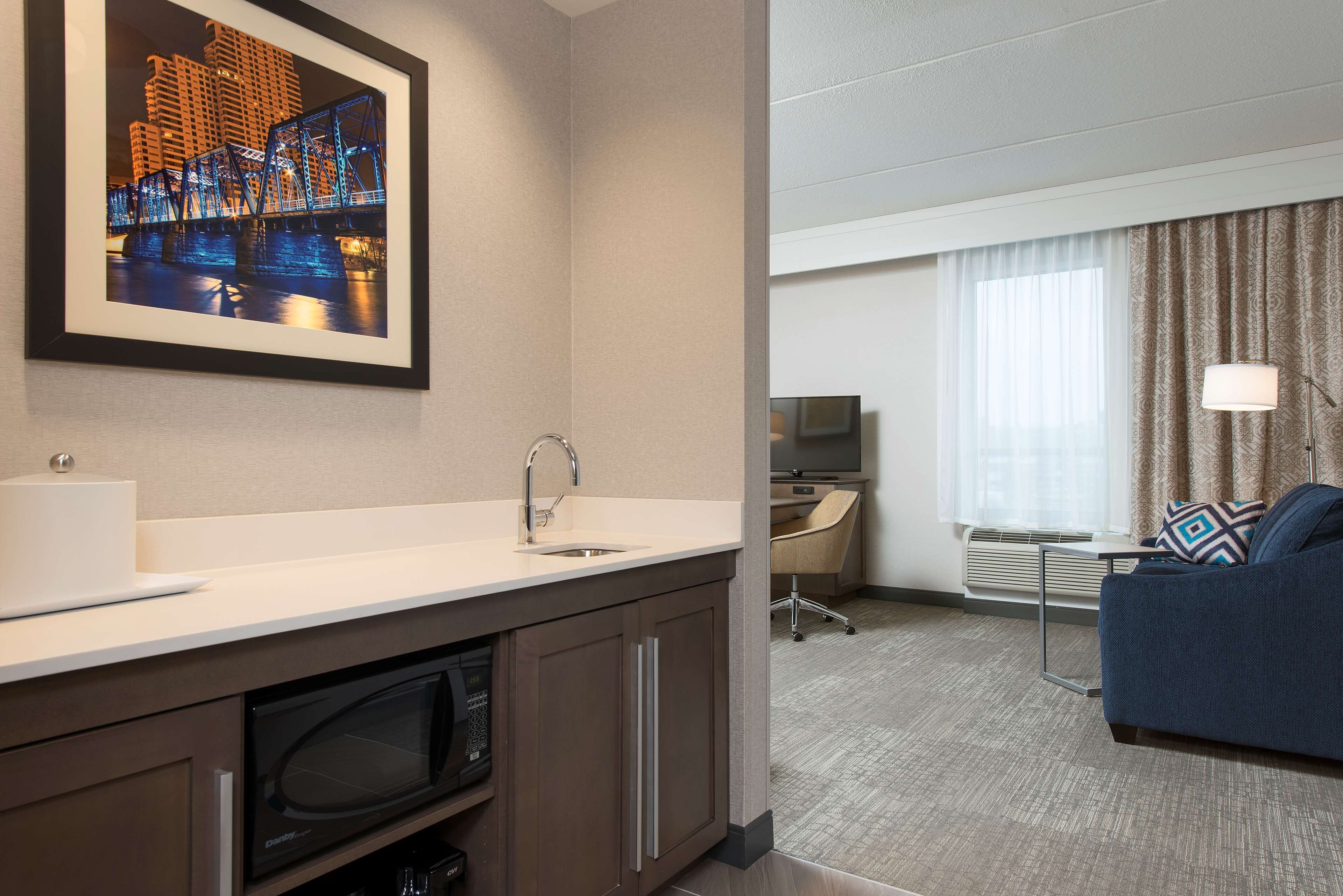 A hotel room with a kitchenette, a large framed picture of a bridge, a sofa, and a TV.