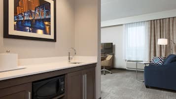 A hotel room with a kitchenette, a large framed picture of a bridge, a sofa, and a TV.