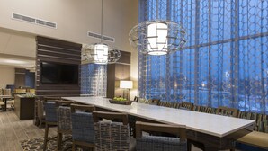A modern dining area with a long table, wicker chairs, and pendant lighting.