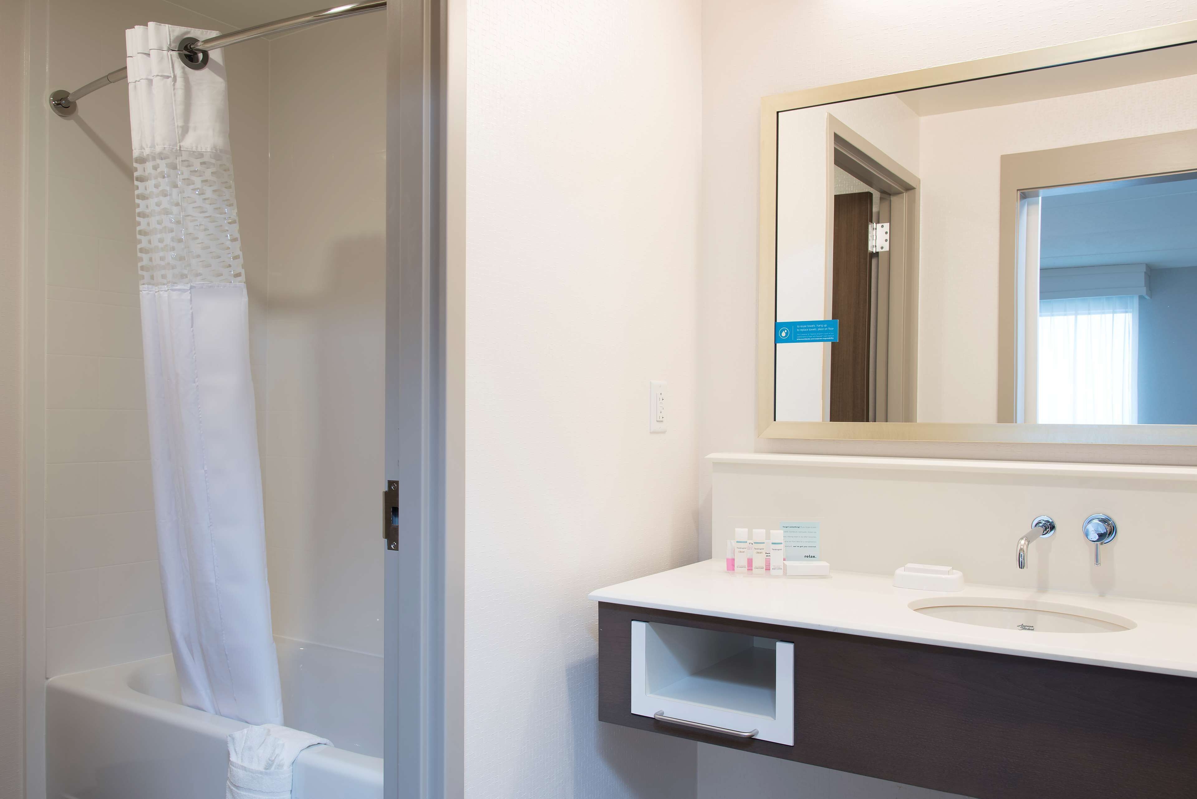 A bathroom with a bathtub, a shower curtain, a sink with a mirror, and toiletries on the counter.