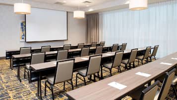 A conference room with multiple tables and chairs, a projector screen, and a large window with curtains.