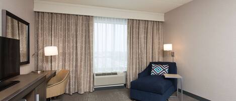 A hotel room with a desk, chair, sofa, and a bed.