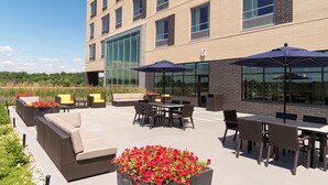 An outdoor patio area with seating and tables, a large window, and a flower planter.