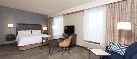 A hotel room with a bed, desk, chair, TV, and a sofa.