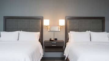 Una habitación de hotel con dos camas, una mesita de noche con lámpara y un cajón pequeño.