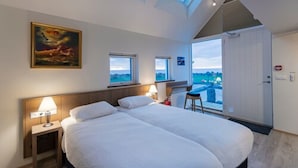 Un dormitorio con una cama grande, dos mesitas de noche con lámparas, un cuadro en la pared y vistas a través de una puerta.