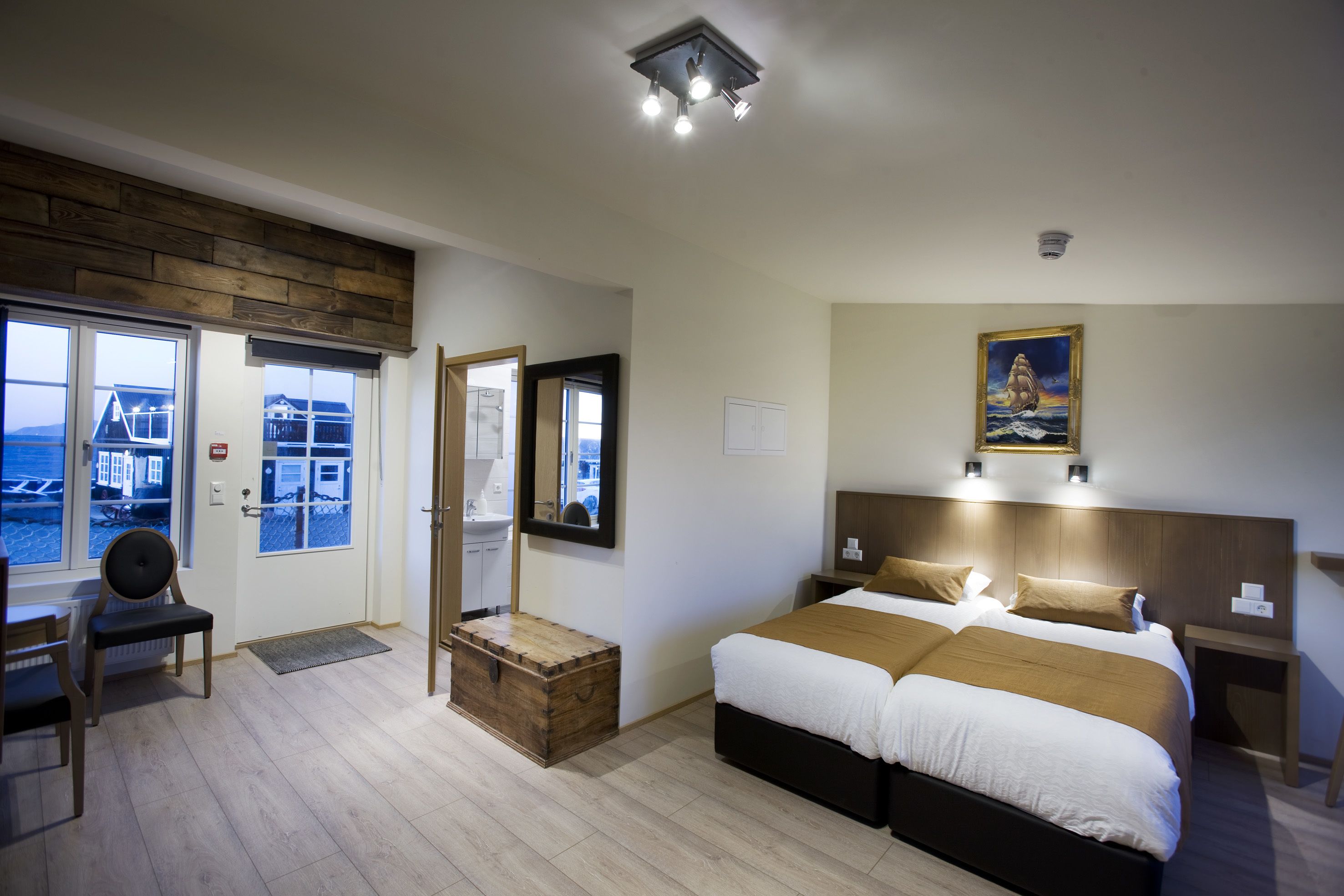 Ett hotellrum med en stor säng, ett skrivbord, en stol, en trälåda och utsikt över havet genom fönstren.
