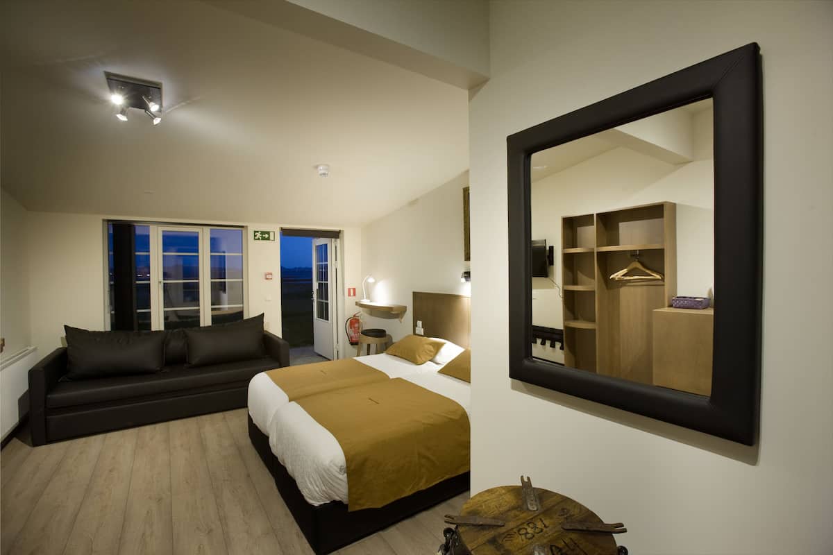 A modern hotel room with a large bed, a sofa, a mirror, and a wardrobe.