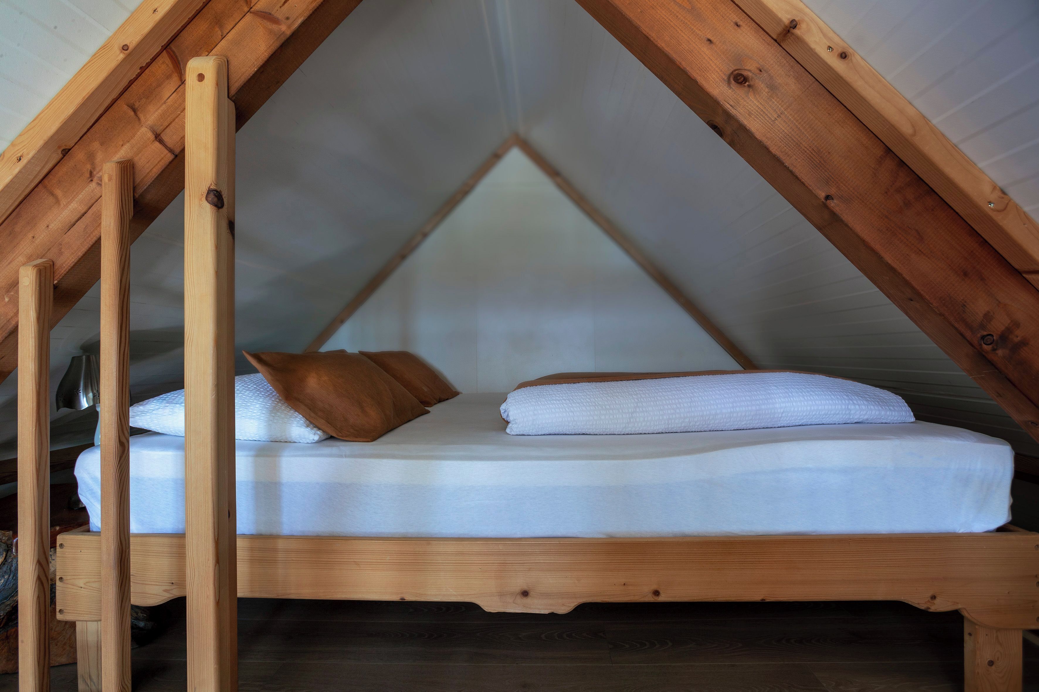 A loft-style bedroom with a wooden bed frame and a sloped ceiling.