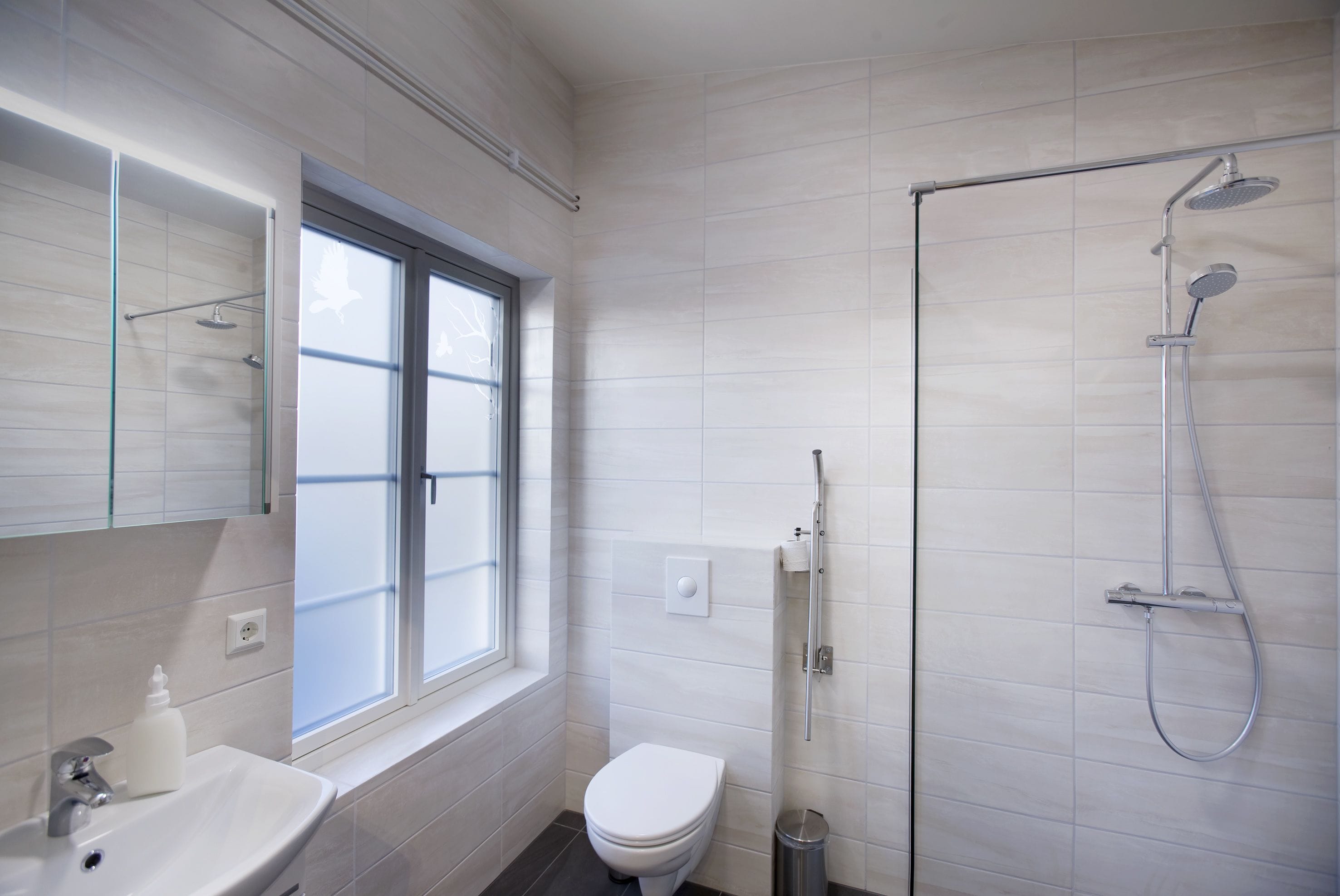 Un baño moderno con inodoro blanco, lavamanos, cabina de ducha de vidrio y ventana que proporciona luz natural.