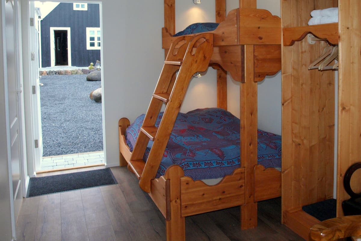 A wooden bunk bed with a ladder, a wooden wardrobe, and a door leading to an outdoor area.