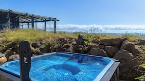 A hot tub with a clear view of the surrounding landscape, including a structure with a mesh roof and a rocky area with vegetation. - Fisherman's Village (Garðabær)