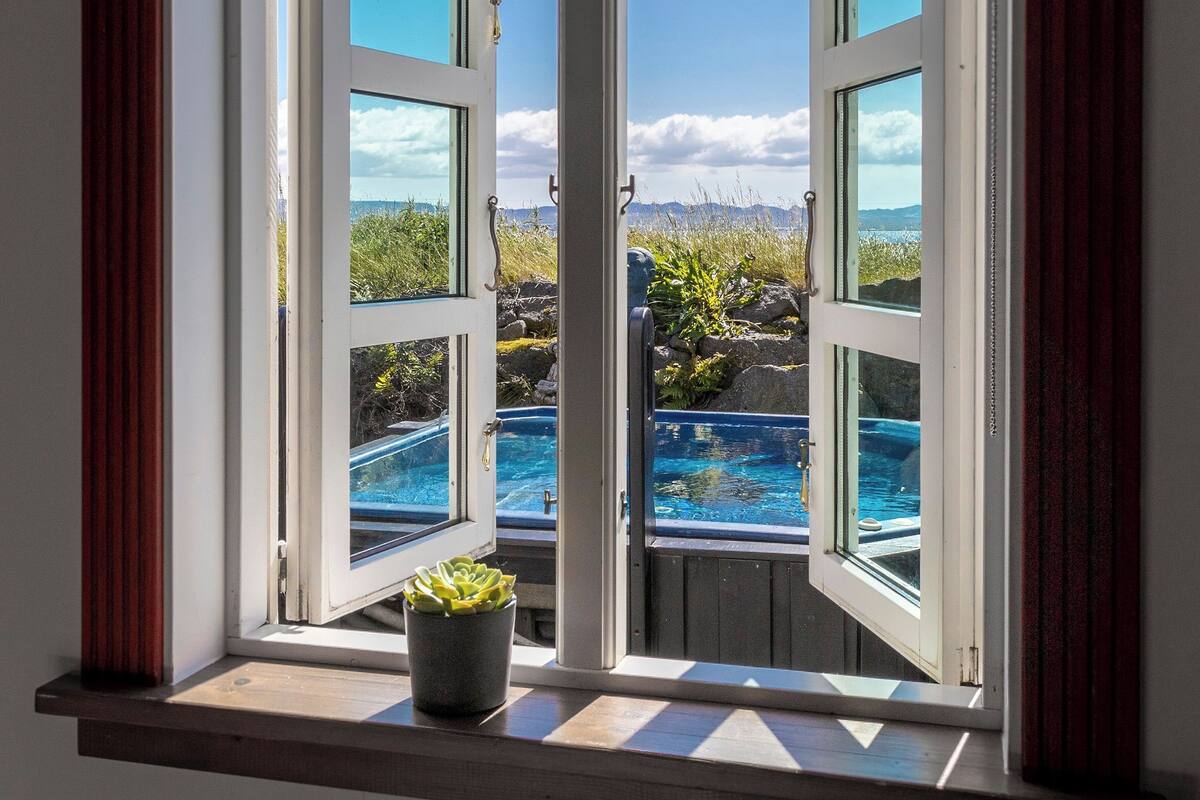 A window with a view of a swimming pool and a mountainous landscape.