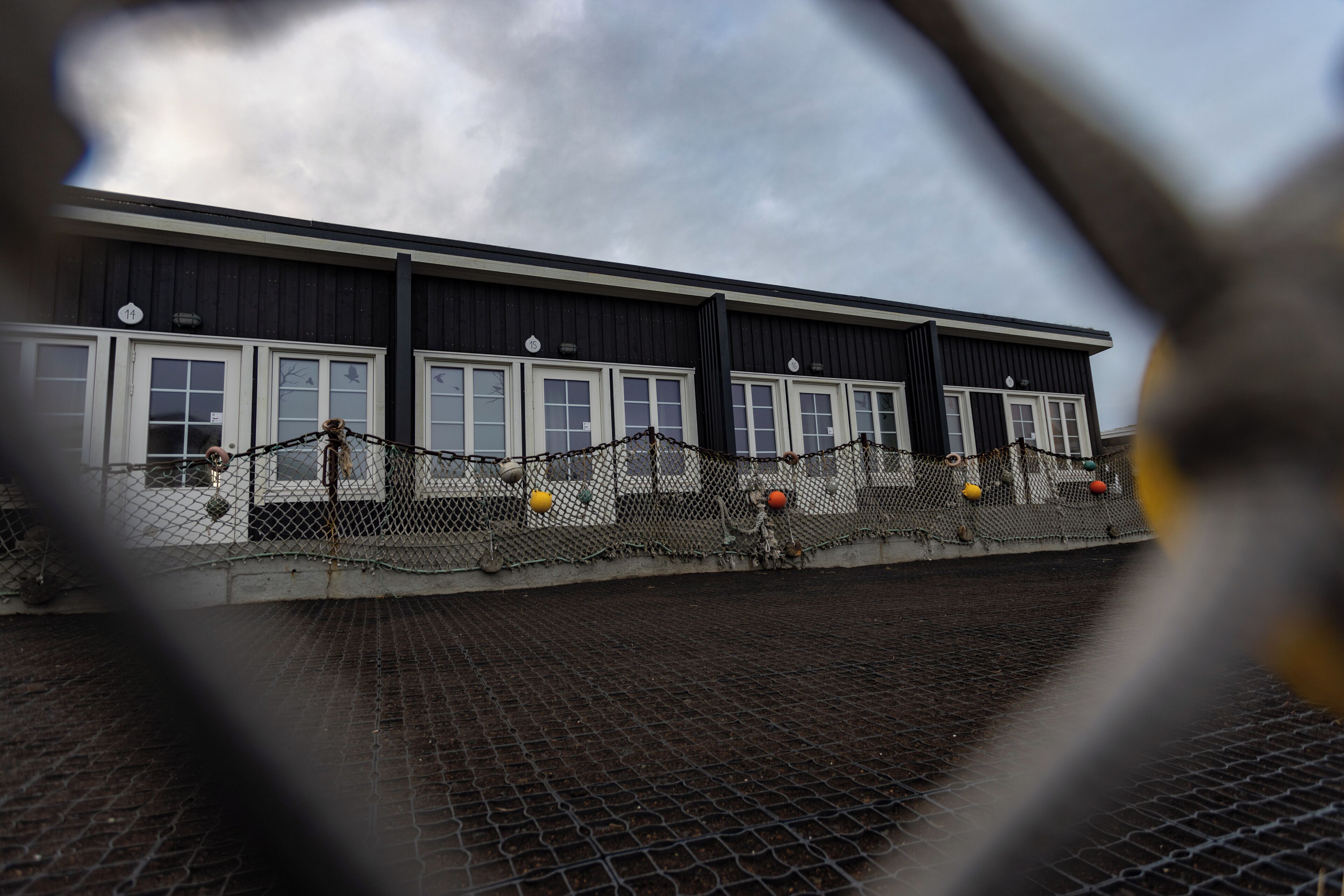 A building with a black facade and white windows, featuring a chain-link fence with colorful balls.