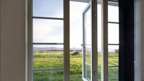 Una habitación con un ventanal que ofrece vistas a un campo cubierto de hierba y montañas distantes.