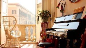 A piano in a room with a balcony, a wicker chair, and a potted plant. - Ca' del Sol (Cagliari)