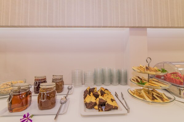 A buffet table with various food items including jars of honey, a plate of brownies, and a tray of fruit. - Hotel Palmyra (Zakynthos)