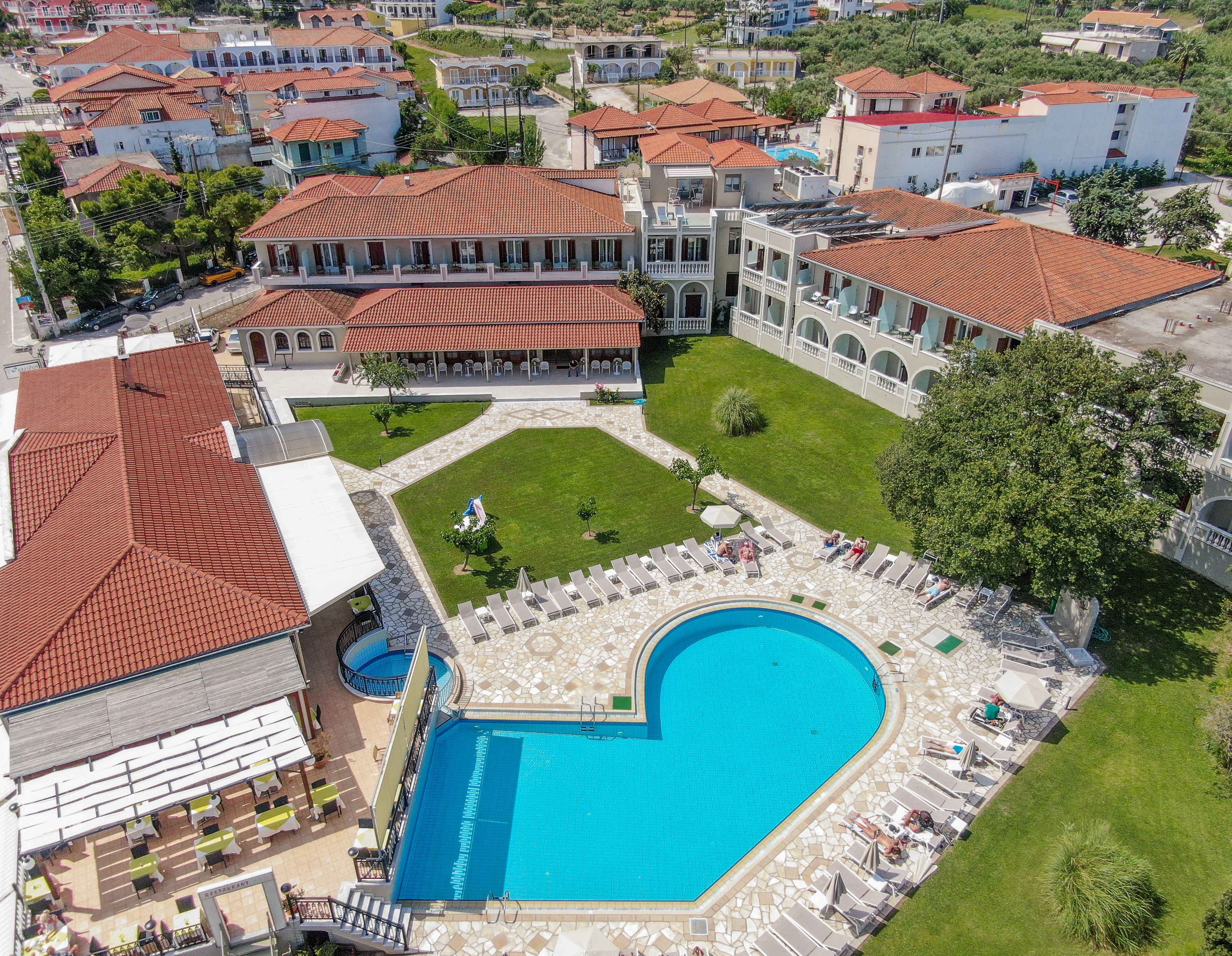 An aerial view of a resort with a large swimming pool, multiple buildings, and a well-maintained lawn.