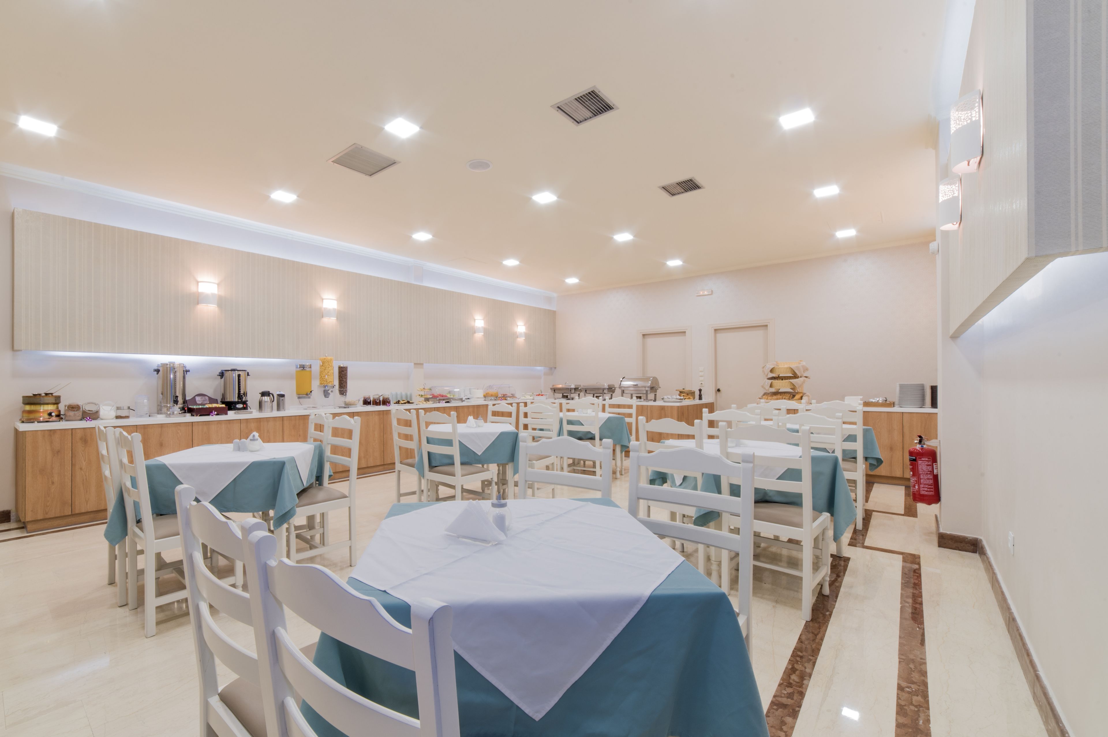 Un comedor con varias mesas y sillas, una cocina con distintos electrodomésticos, y un extintor de incendios en la pared.