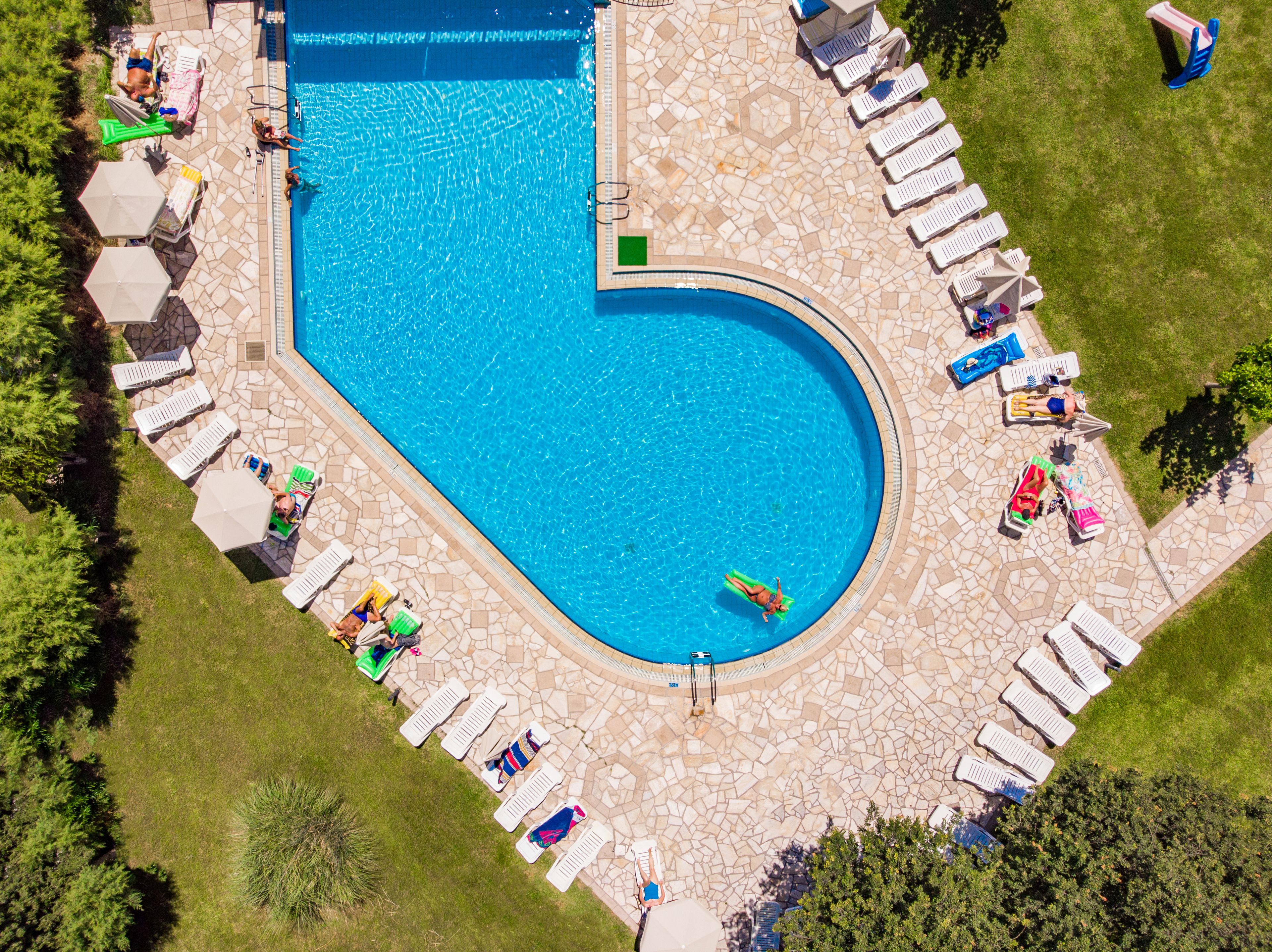 An aerial view of a swimming pool with a unique heart-shaped design, surrounded by lounge chairs and umbrellas.