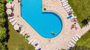 An aerial view of a swimming pool with a unique heart-shaped design, surrounded by lounge chairs and umbrellas.