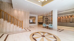 Un vestíbulo amplio con suelo de mármol, una escalera de madera y una zona de estar con sillones.