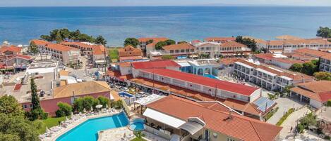 Une station balnéaire dotée d’une piscine, de plusieurs bâtiments aux toits recouverts de tuiles rouges et offrant une vue sur la mer.