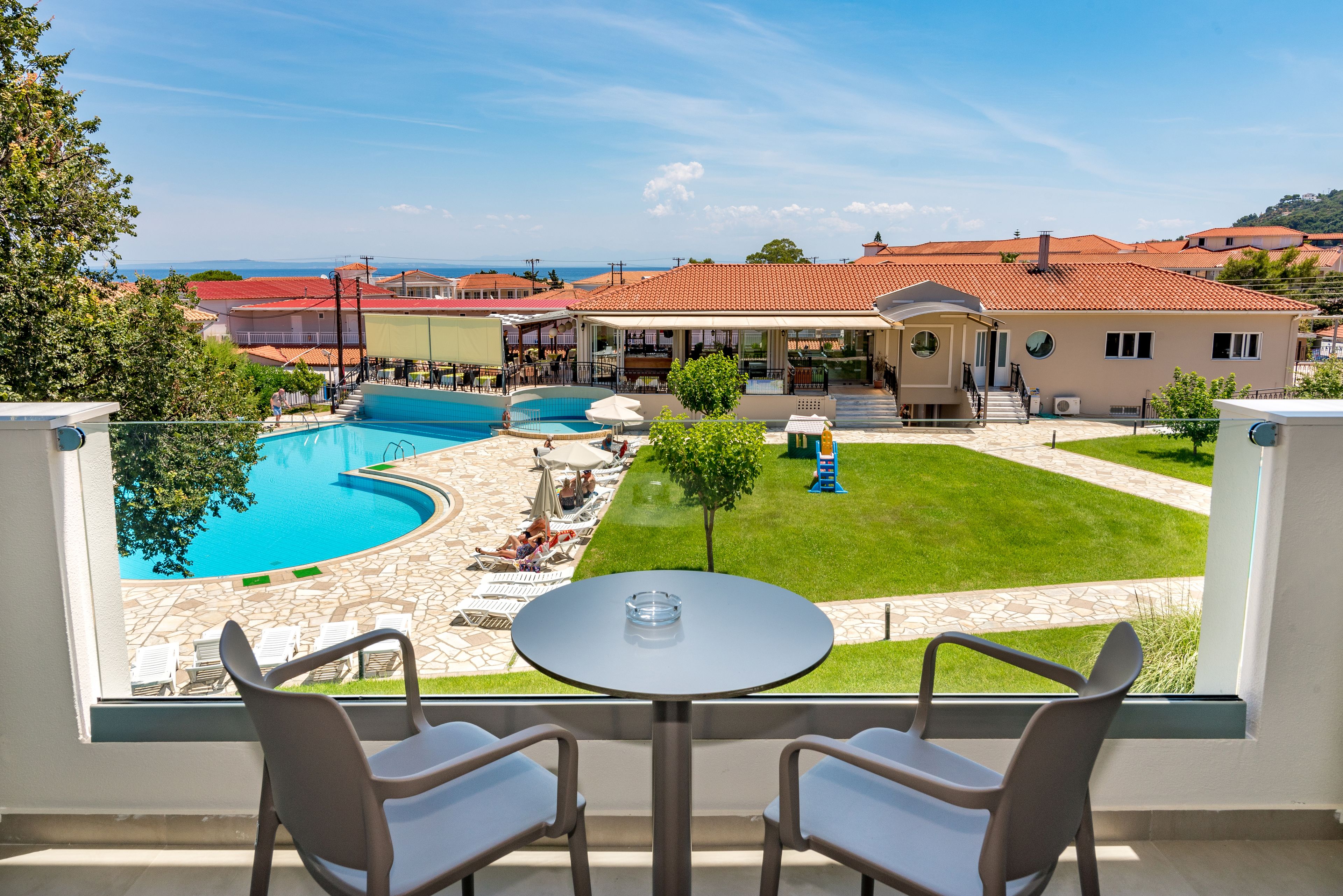 A balcony with a table and chairs overlooking a swimming pool and a grassy area with lounge chairs.