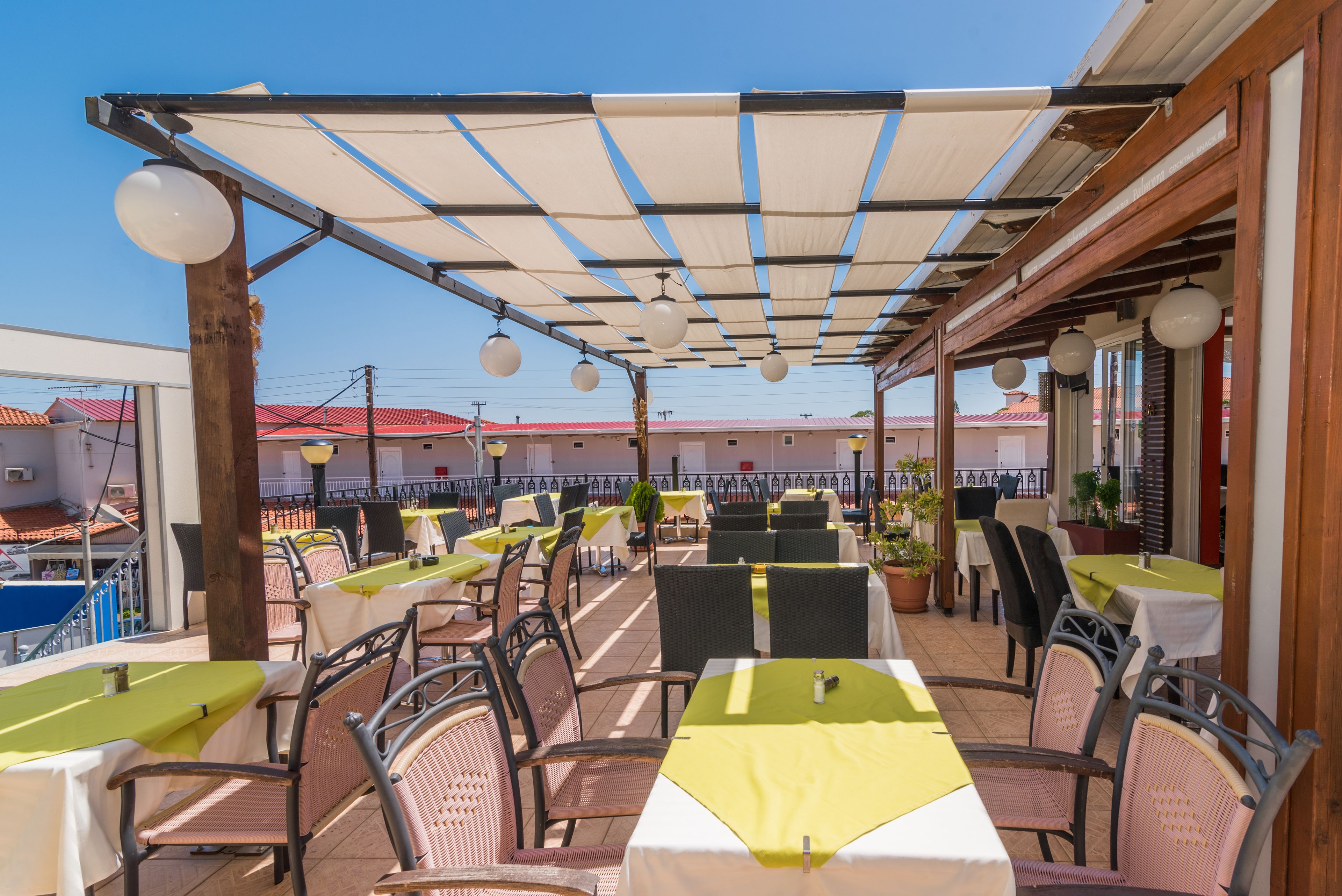 Una terrazza esterna con tavoli e sedie, riparata da un tettoia, con vista su un edificio dai tetti rossi.