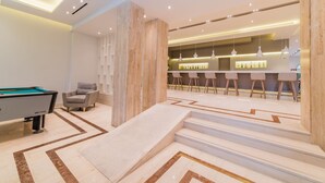 Un área de bar moderna con mesa de billar, taburetes y una escalera que lleva a la barra.