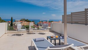 Un balcón con dos sillones de relax, una mesita con una bebida y vistas al mar y edificios.
