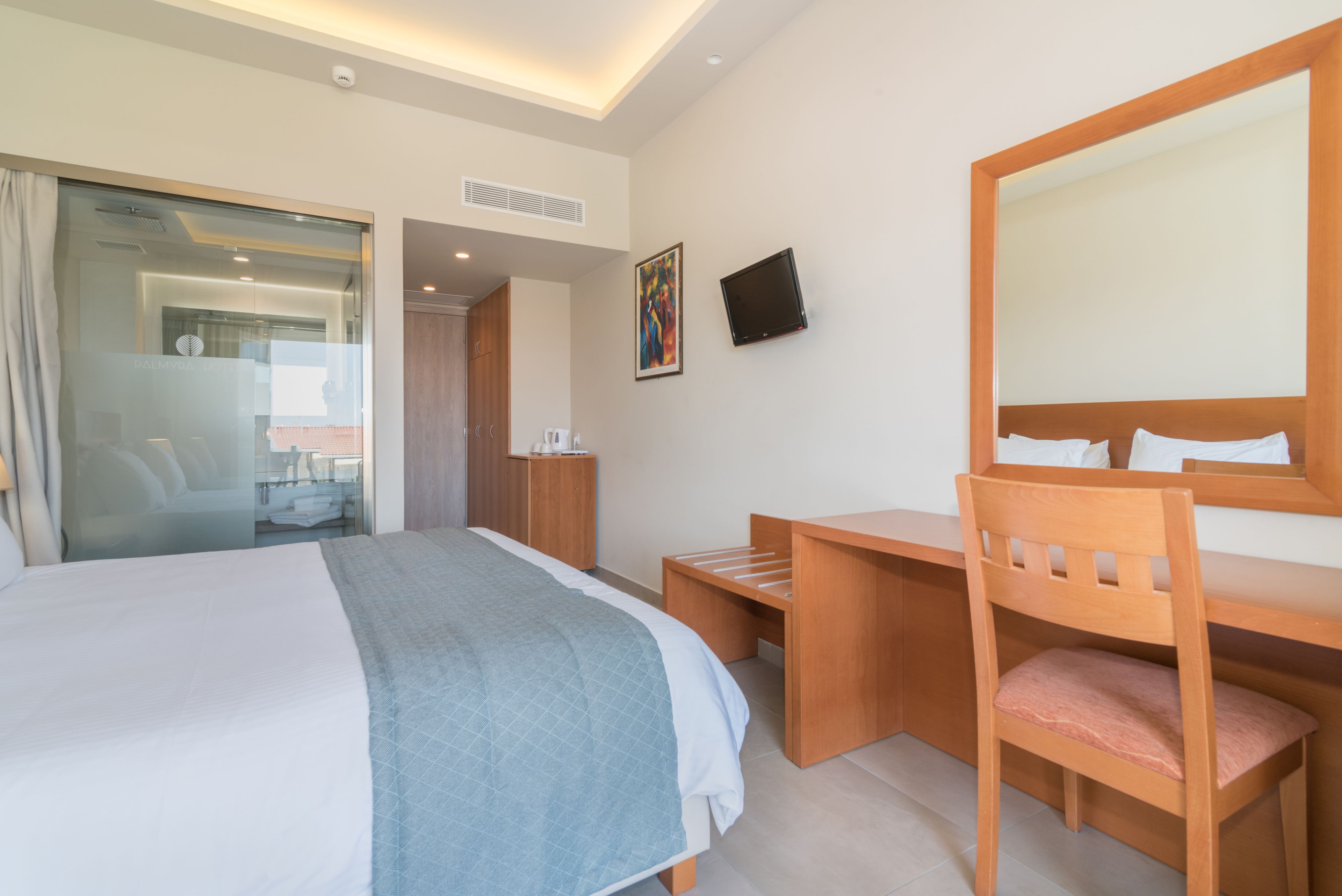 A hotel room with a large bed, a desk, a chair, a TV, and a door leading to a bathroom.