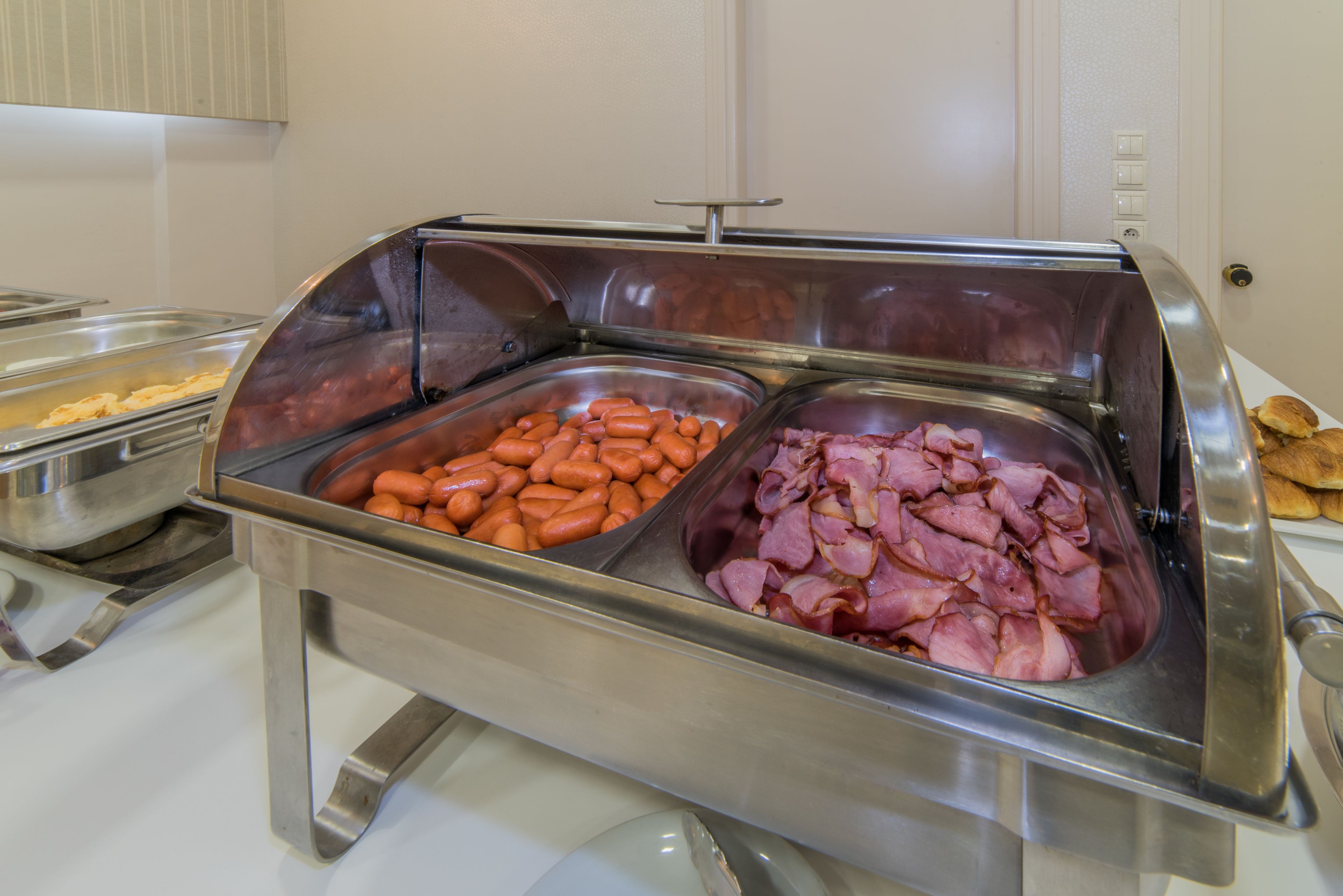 A buffet with three stainless steel chafing dishes containing different types of food.