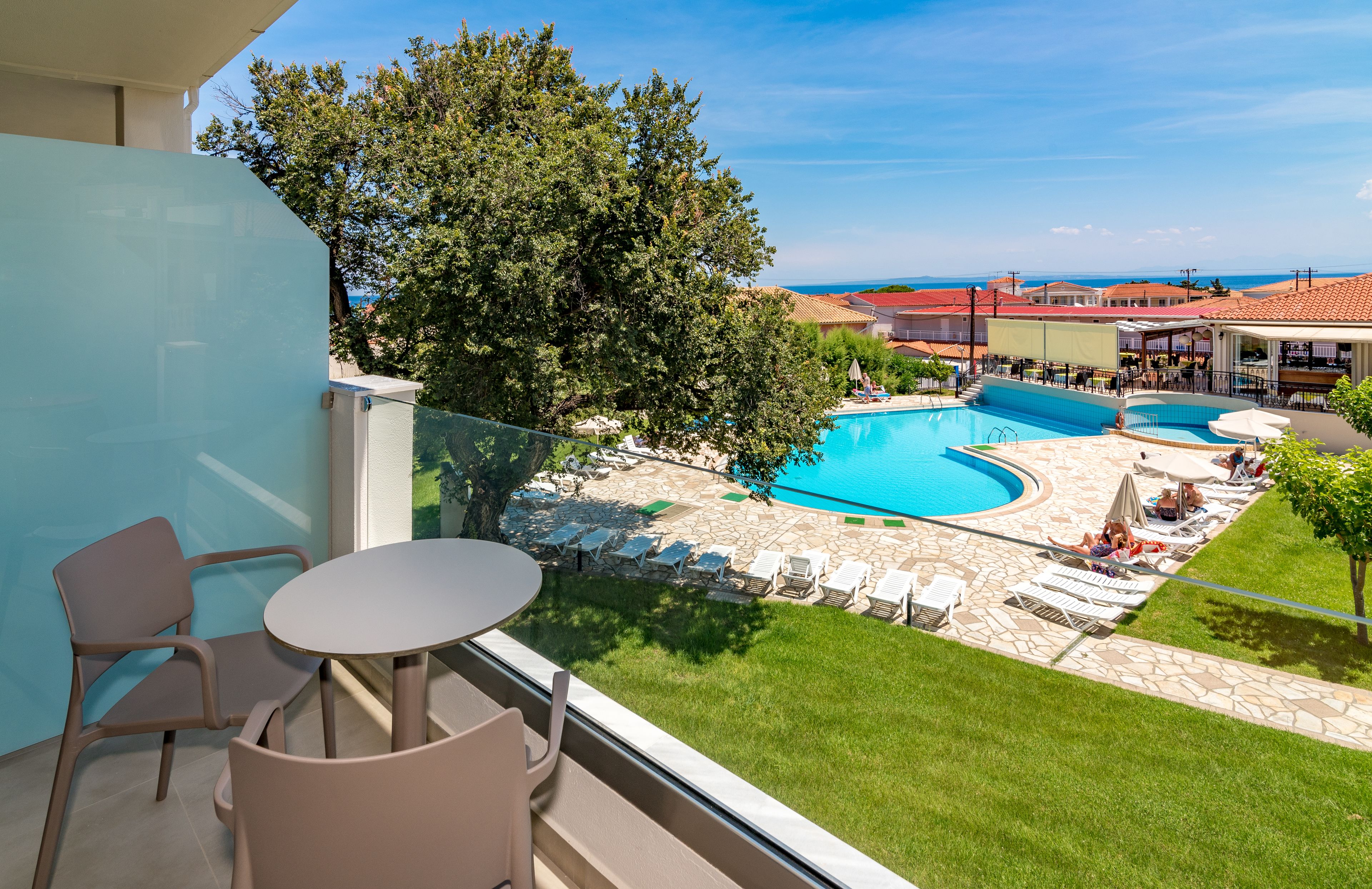 En balkon med udsigt over en swimmingpool, liggestole og en græsplæne.