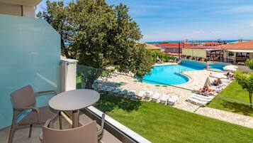 En balkon med udsigt over en swimmingpool, liggestole og en græsplæne.