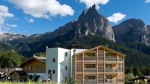 A mountain lodge with a modern design, featuring a prominent wooden facade and a white building in the foreground. - Hotel Arvina (Castelrotto)
