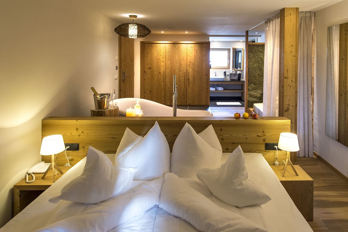 Habitación de hotel con una cama grande, cabecera de madera, lámparas de noche, mesita de noche de madera, un espejo y vistas al baño.