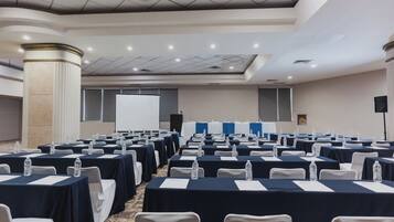 Un salón de conferencias con filas de mesas, sillas y botellas de agua.