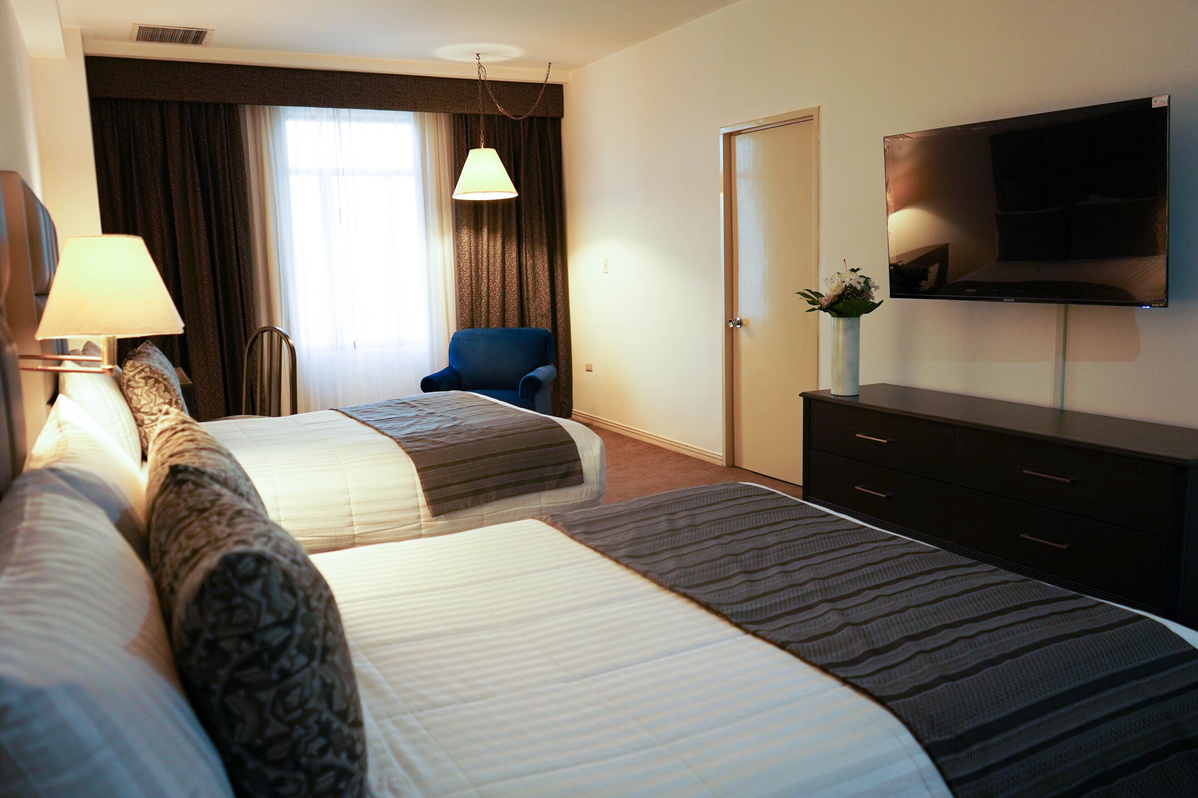 Habitación de hotel con dos camas, un escritorio, una silla, un televisor y una ventana con cortinas.
