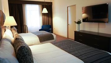 Habitación de hotel con dos camas, un escritorio, una silla, un televisor y una ventana con cortinas.