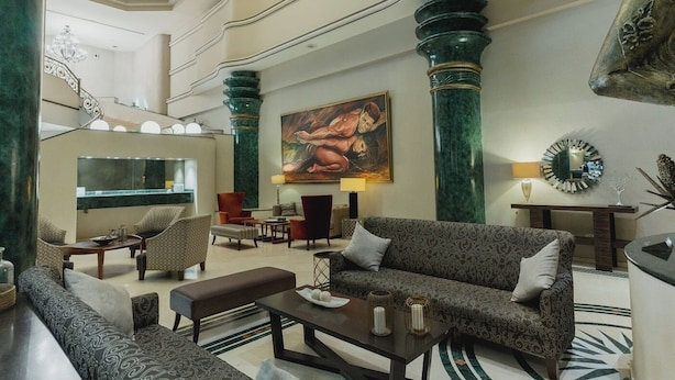 A spacious lobby with high ceilings, a chandelier, a large painting, and a modern fireplace. - Hotel San Marcos Grand (Culiacán)