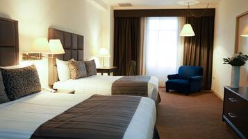 A hotel room with two beds, a chair, a dresser, and a large window with curtains.