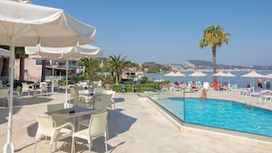 Zona junto a la piscina con sombrillas blancas, sillas de descanso y vista despejada al mar.