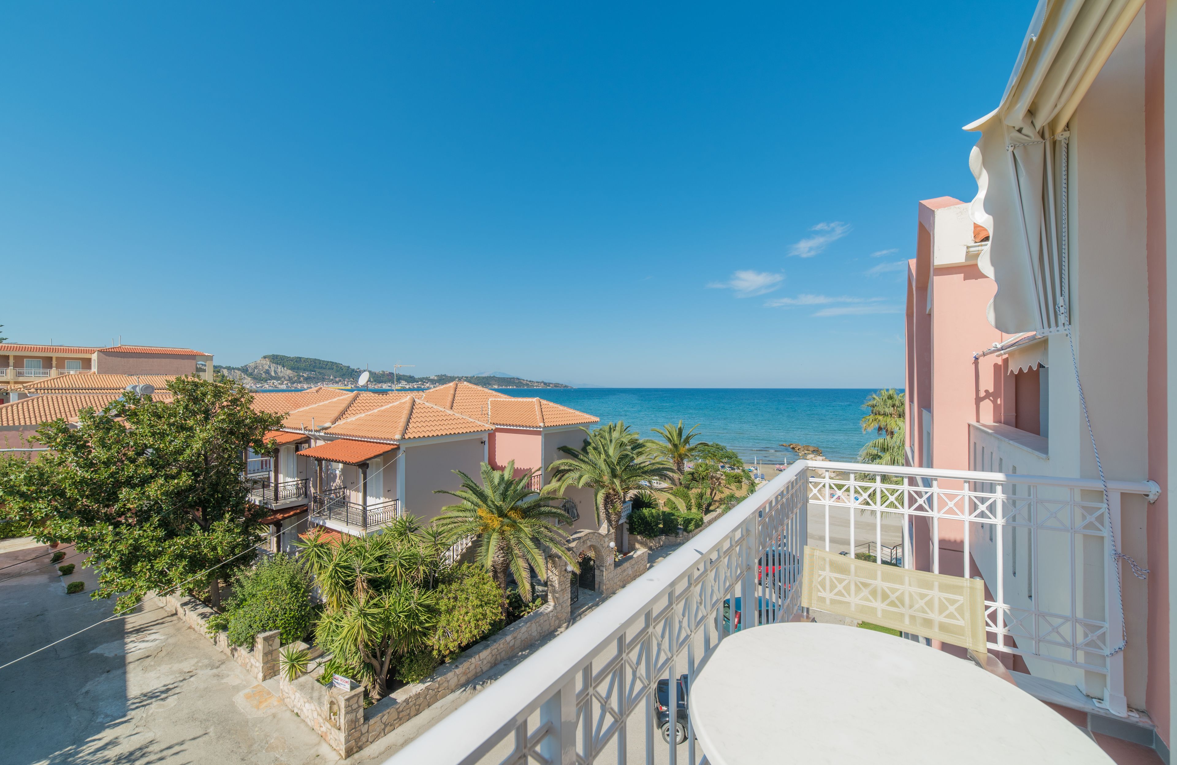 Un balcón con vista al mar, un edificio con techo de tejas y una palmera.