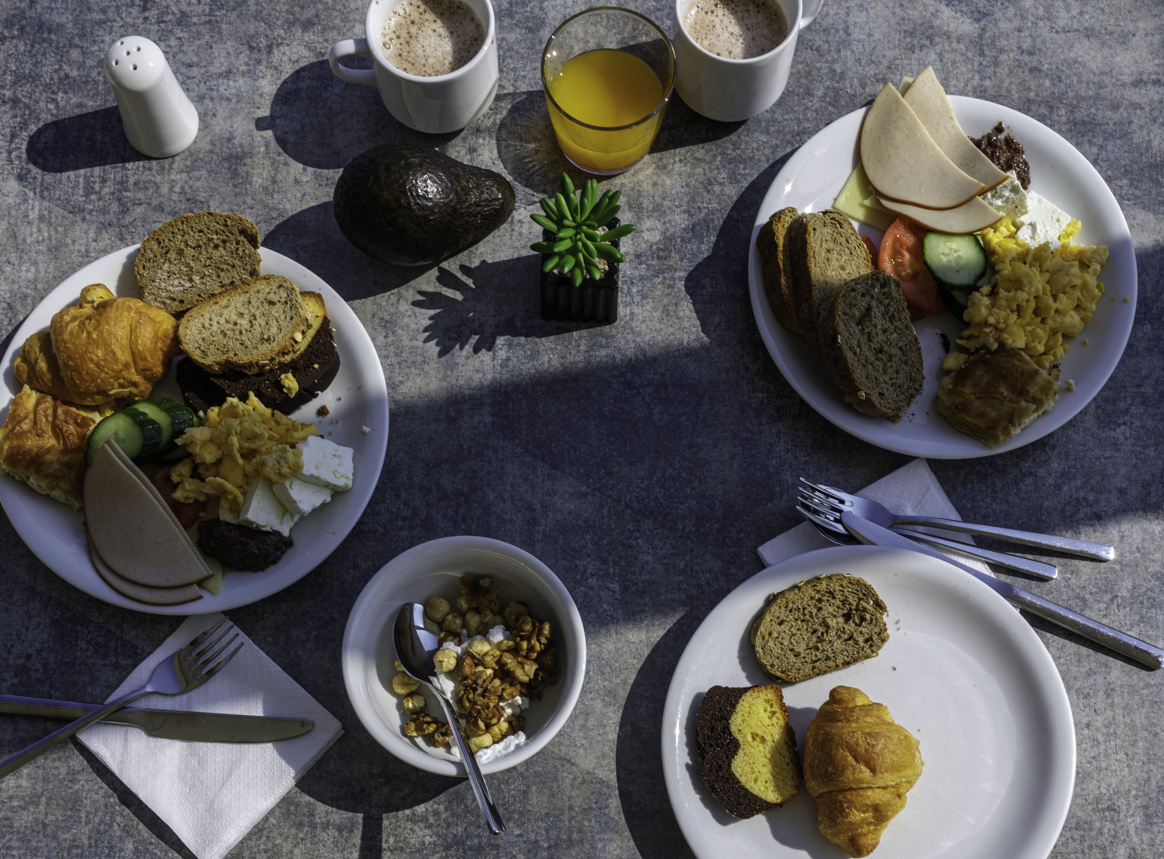 A table with breakfast plates containing croissants, bread, eggs, and vegetables. There are also two cups of coffee and a glass of orange juice.
