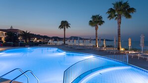 Una piscina de borde curvo, rodeada de palmeras y sillas de playa.