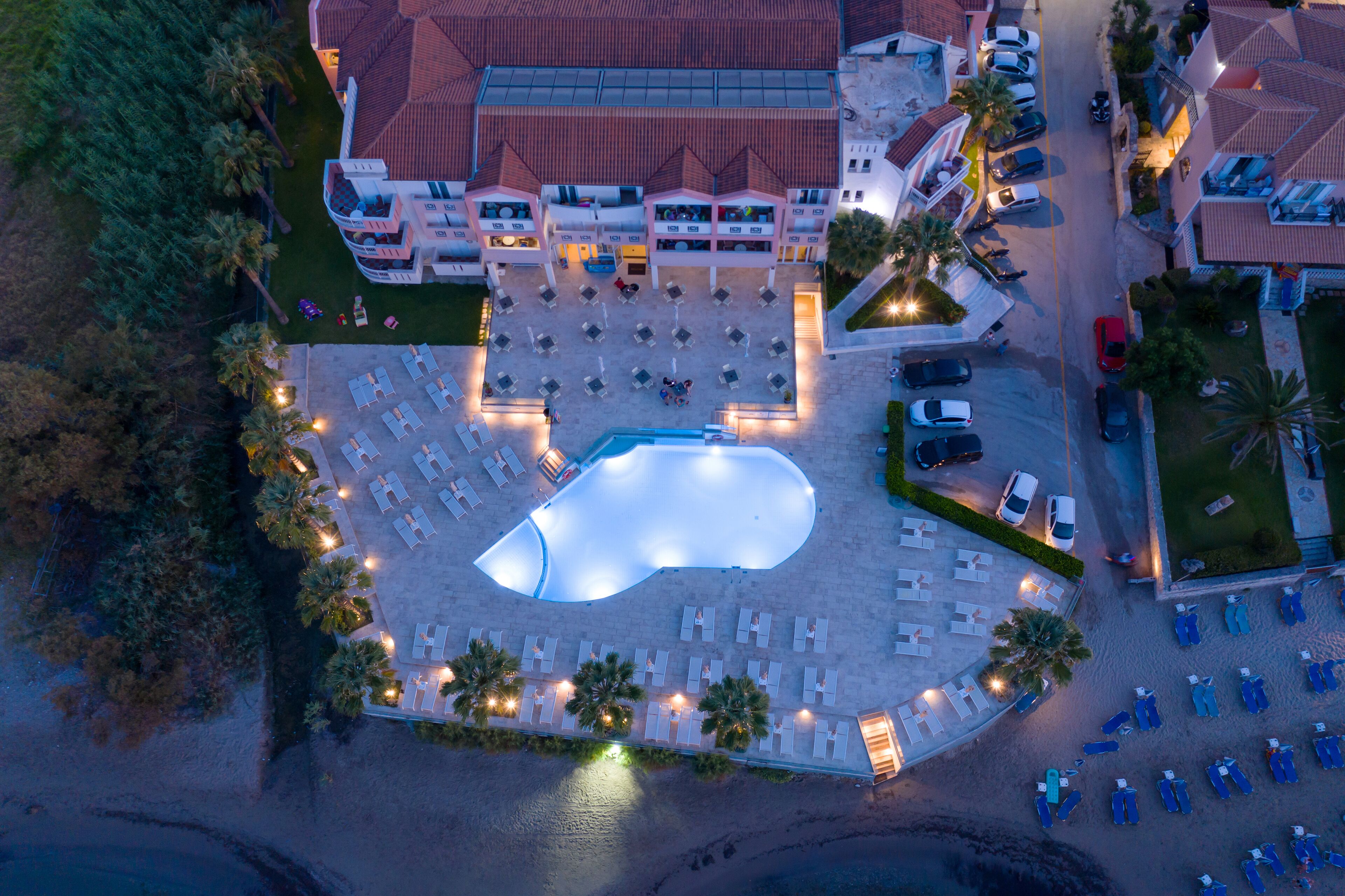 An aerial view of a hotel with a swimming pool, multiple floors, and a parking area.