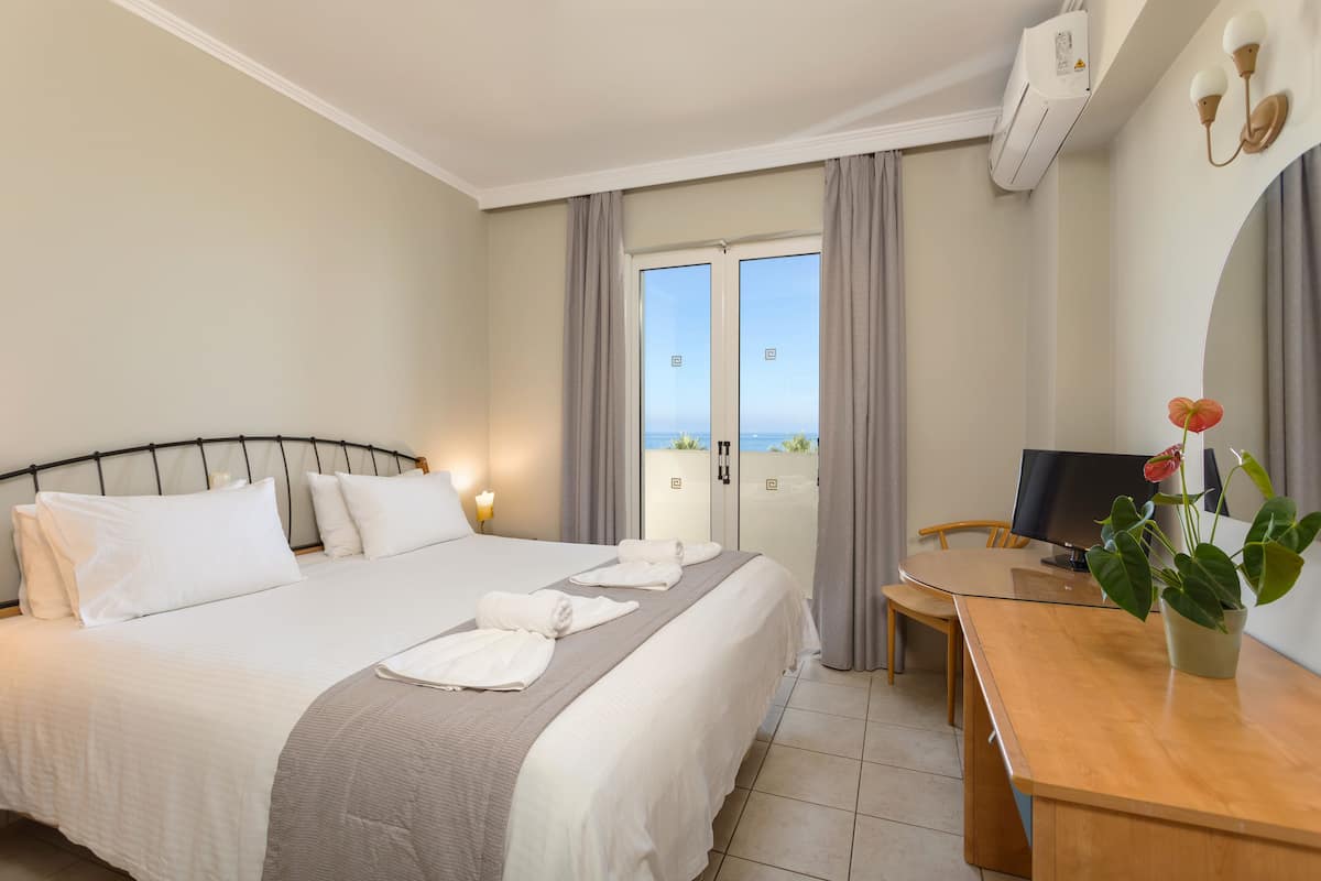 Habitación de hotel con cama, escritorio, televisión y balcón con cortinas.